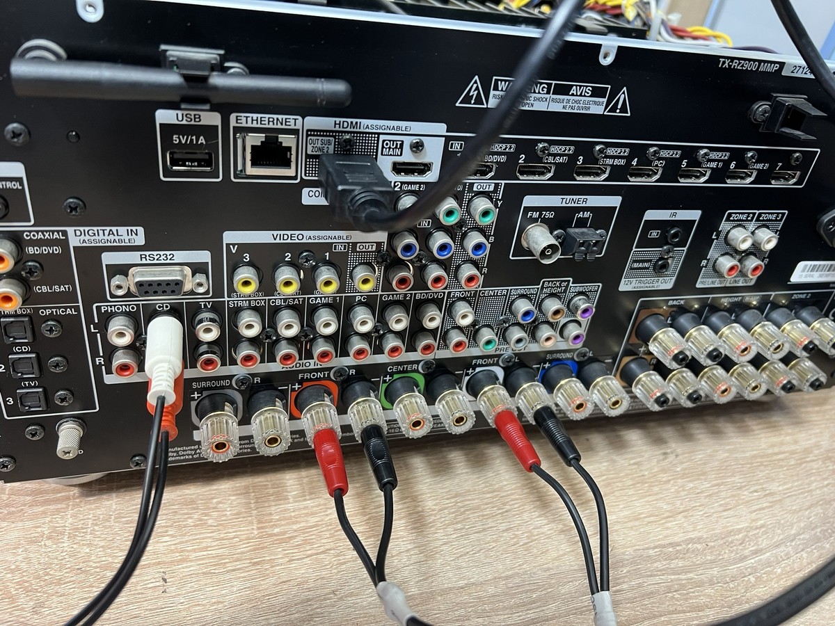 Tył amplitunera kina domowego z widocznymi zaciskami głośnikowymi, złączami wejściowymi i podłączonymi kablami